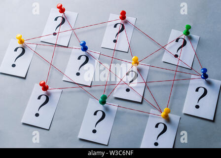 Réseau de points d'interrogation imprimés sur cartes blanches épinglées avec punaises et rejoint par chaîne dans un cadre conceptuel de l'image sur fond gris Banque D'Images