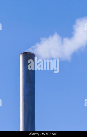 Le tuyau de presse de la fumée dans le ciel bleu et pollue l'environnement. Problème écologique. Banque D'Images