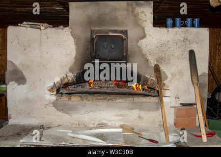 Face avant d'un four à pain au feu de bois avec un feu brûlant et d'outils pour faire du pain plat, photo du nord de la Suède. Banque D'Images