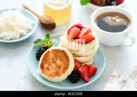 Beignets au fromage blanc, fromage ou syrniki crêpes avec les fraises, le miel et une tasse de café. Délicieux petit déjeuner sain Banque D'Images