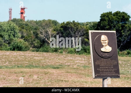 Une plaque de bronze usé posté par la National Aeronautics and Space Administration (NASA) à la John F. Kennedy Space Center en Floride, USA, rend hommage à John H. Glenn Jr., avec une inscription : "Le premier Américain à voyager autour de la planète a commencé ses trois-orbite de vol de ce complexe de lancement dans l'amitié de 7 Atlas Mercure no 6 à 9:47 AM 20 février 1962. Le Mercure du projet a été une étape cruciale sur l'homme en son voyage vers la lune." Dans l'arrière-plan sont 2 pylônes utilisés pour le lancement de fusées avec leurs charges utiles dans l'espace. Centre Spatial Kennedy a été le principal site de lancement de la NASA depuis 1968. Banque D'Images