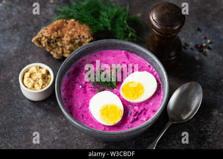 Soupe de betteraves froide avec un œuf dans un bol en céramique sur fond sombre Banque D'Images