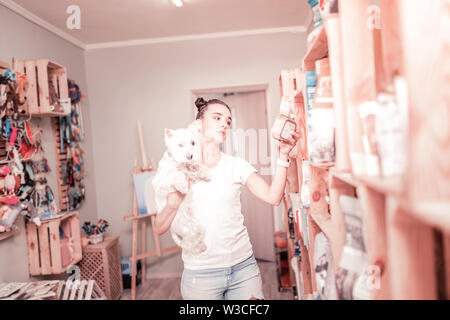 Choix des aliments. Dark-haired young woman with white dog choisissent des aliments dans la boutique pour son animal de compagnie Banque D'Images