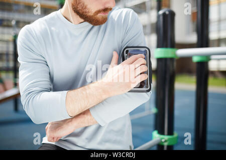 Close-up of red graves-barbu dans sweater debout sur un terrain de sport et la fixation en cas d'épaule sur smartphone Banque D'Images