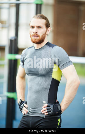 Portrait de l'athlète masculin en sueur fatigue grave avec beard wearing sports Hirt et gants sans doigts tenant les mains sur les hanches à l'extérieur Banque D'Images