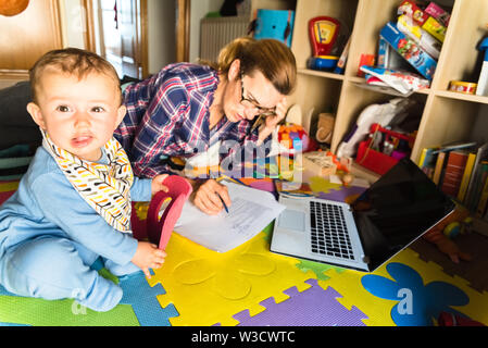 Mère de travailler sur son ordinateur tout en prenant soin de son bébé à la maison, le multitâche femme, concept du travail féminisme et éducation. Banque D'Images