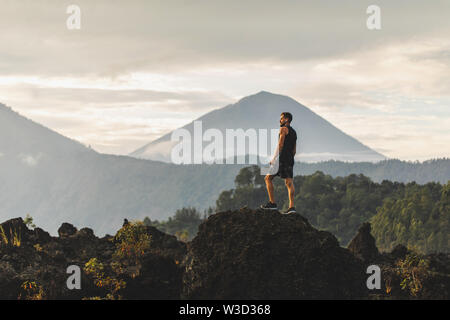 Jeune homme debout sur le dessus de la pierre et bénéficiant d'une vue sur la montagne volcanique Agung à Bali. Billet d'active et en concept. Banque D'Images