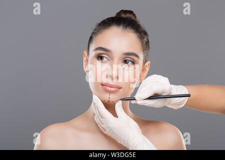 Jeune femme médecin marquant le visage avant de la chirurgie cosmétique Banque D'Images