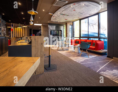 Saint-Gratien, France - Jul 15, 2018 : point de vue d'ensemble de l'intérieur du hall de l'hôtel Ibis avec tables vides et zone de repos zone avec de large et grande fenêtre à la gare centrale Banque D'Images