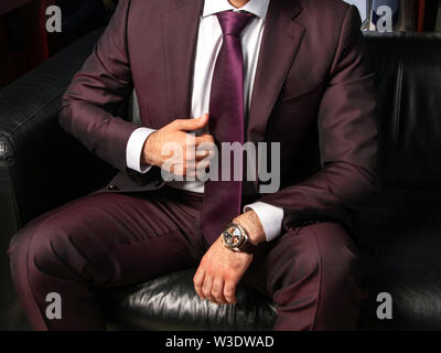 Un homme dans un costume classique est assis sur un canapé en cuir noir, close-up. Costume hommes designers italiens. Personne d'affaires de l'habillement. Les montres de Brown. Les hommes" Banque D'Images
