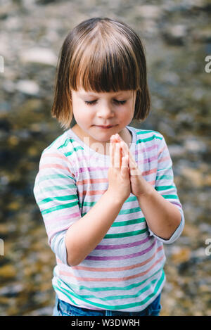 Petite fille de prier avec les yeux fermés sur la rive d'un ruisseau de montagne Banque D'Images