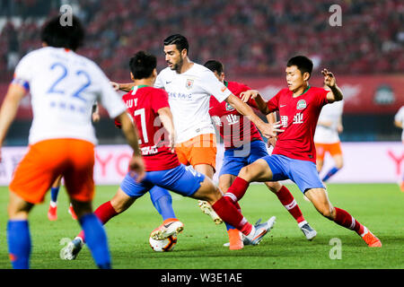 Un joueur de football italien Graziano Pelle, centre, de Shandong Luneng Taishan passe le ballon contre des joueurs de Henan Jianye dans leur 17e match au cours de l'Association de football chinoise 2019 Super League (CSL) dans la ville de Zhengzhou, province du Henan en Chine centrale, le 12 juillet 2019. Henan Shandong Luneng Taishan Jianye défait 3-2. Banque D'Images