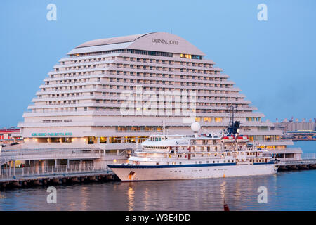 L'hôtel Oriental sur front de Kobe au Japon au cours de l'heure bleu crépuscule. Petit bateau de croisière, l'esprit des océans, amarré à l'avant. Ciel bleu pâle. Banque D'Images