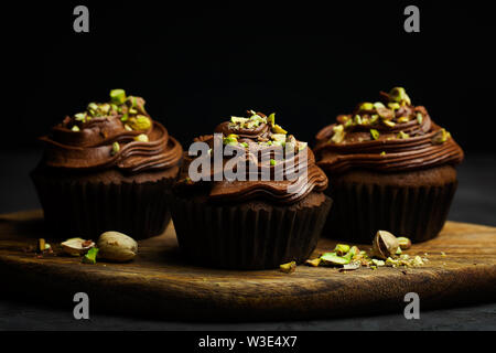 De beaux petits gâteaux au chocolat garnie de crème au beurre au chocolat pistache décoré sur fond sombre close-up avec copie espace pour le texte Banque D'Images