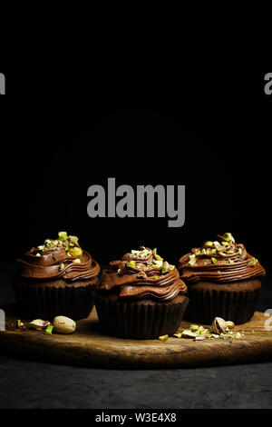 De beaux petits gâteaux au chocolat garnie de crème au beurre au chocolat pistache décoré sur fond sombre close-up avec copie espace pour le texte Banque D'Images