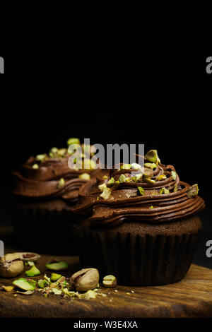 De beaux petits gâteaux au chocolat garnie de crème au beurre au chocolat pistache décoré sur fond sombre close-up avec copie espace pour le texte Banque D'Images