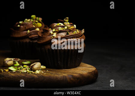De beaux petits gâteaux au chocolat garnie de crème au beurre au chocolat pistache décoré sur fond sombre close-up avec copie espace pour le texte Banque D'Images