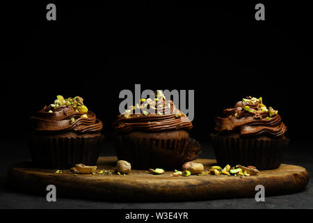 De beaux petits gâteaux au chocolat garnie de crème au beurre au chocolat pistache décoré sur fond sombre close-up avec copie espace pour le texte Banque D'Images