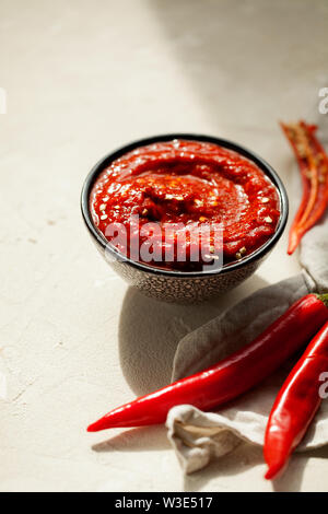 Rose traditionnel fait maison-harissa piment pâte de sauce à l'ail et l'huile d'olive dans un petit bol sur fond de plâtre blanc with copy space Banque D'Images