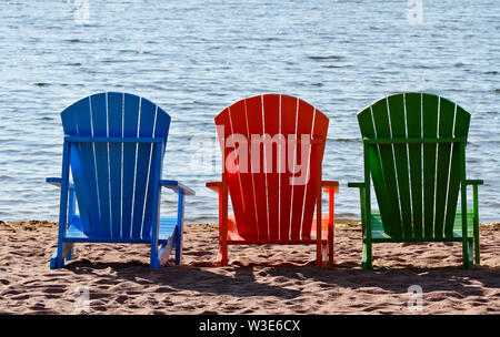 Trois chaises de couleur différente sur une plage vide dans la soirée Banque D'Images