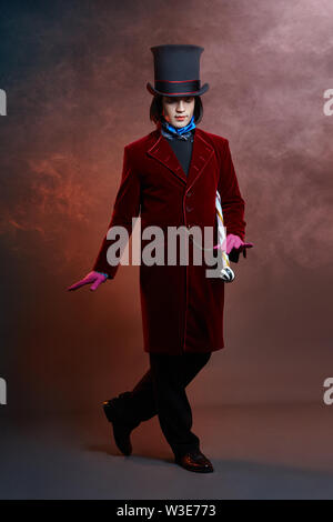 L'homme cirque fabuleux dans un chapeau et un costume rouge posant dans la fumée de couleur sur un fond sombre. Un clown lors d'une fête, l'homme représentant d'un conte de fées. Wiz Banque D'Images