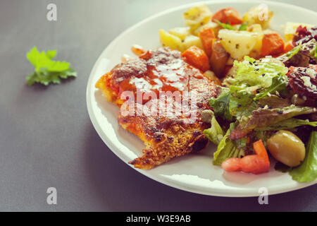 Filet de poisson gratiné au fromage avec pommes de terre, patates douces, carottes et légumes verts et mélanger. Vinaigrette Sel frais assaisonnés et saupoudrés de Banque D'Images