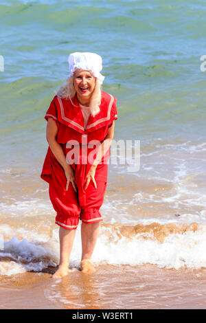 Festival annuel de Broadstairs Dickens. Beach Party victorienne. Senior woman in red Victorian maillot paddling, face viewer et rire. Banque D'Images