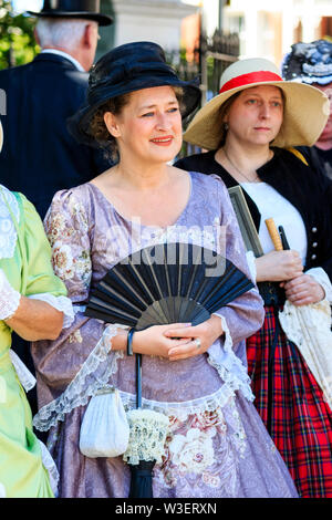 Broadstairs Dickens Festival. Les femmes mûres portant une robe mauve ère victorienne avec chapeau noir et muni d'un ventilateur noir. Souriant, pas de contact visuel. Banque D'Images