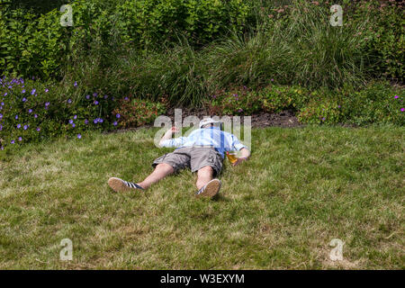 L'homme évanoui sur l'herbe banque avec verre de bière dans la main à Wimbledon 2019 Banque D'Images