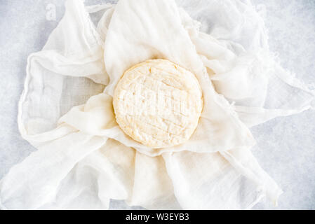 Fromage de vache doux ronde sur tissu de mousseline blanche et bleu fond à motifs. Vue d'en haut. Banque D'Images