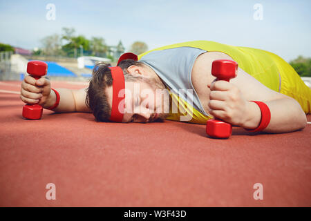 Fat lazy man sleeps fatigué se trouve sur la piste dans le stade. La notion de perte de poids, le régime alimentaire. Banque D'Images