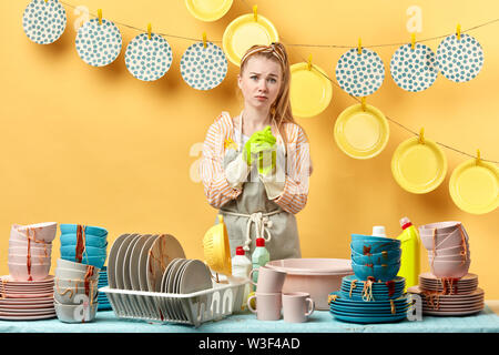 Triste Malheureux femme tenant ses mains et posant pour l'appareil photo. fatigué girl ne peut pas trouver bon plat de savon. isolé sur fond jaune, studio shot. Banque D'Images