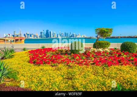 Paysage de printemps des fleurs et arbres en fleurs sur la promenade de la Corniche de la baie de Doha au Qatar. Haut gratte-ciel du centre-ville de Doha sur la distance Banque D'Images