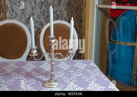 Trois bougies blanches sur la table . trois bras candle stick support, deux candélabres au sommet, au-dessus de meubles, de coupe contre mur blanc dans la salle de séjour, Banque D'Images