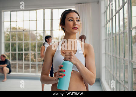 Assez jeune femme prend une pause à partir de sa classe de yoga à boire à sa bouteille d'eau. Banque D'Images