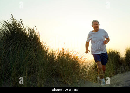 Senior man jogging jusqu'Une dune de sable au coucher du soleil. Banque D'Images