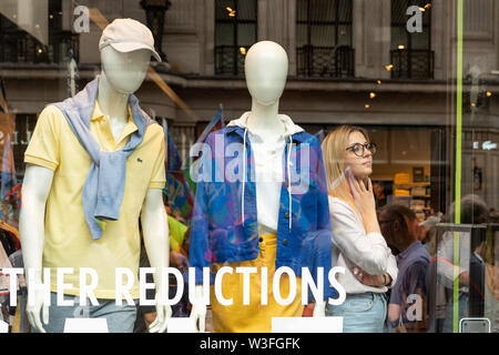 6 juillet 2019 - Londres, Royaume-Uni. Employé de magasin féminin curieusement regarder par la fenêtre tout en se tenant près de deux mannequins. Banque D'Images