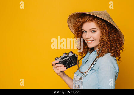 Cute traveler en chapeau chinois avec appareil photo rétro sur fond jaune Banque D'Images