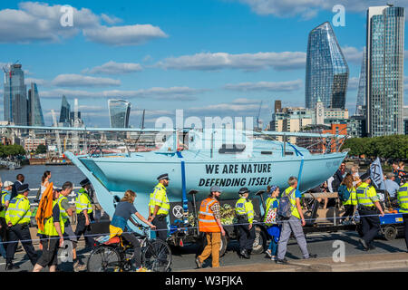 Londres, Royaume-Uni. 15 juillet 2019. Le bateau est remorqué sur Waterloo Bridge par un remorqueur électrique Extinction - bloc de rébellion à l'extérieur de la rue Fleet la Royal Courts of Justice dans le cadre d'un nouveau cycle de manifestations de l'environnement, avec leur nouveau bateau bleu le Polly Higgins - du nom d'une femme qui est morte du cancer sur la protestation avril tout en faisant la promotion de son idée d'un écocide droit. Ils sont une nouvelle fois en lumière l'urgence qu'ils croient qu'il y a seulement 11 ans avant qu'il ne soit trop tard pour épargner à leurs enfants un climat de catastrophe. Crédit : Guy Bell/Alamy Live News Banque D'Images