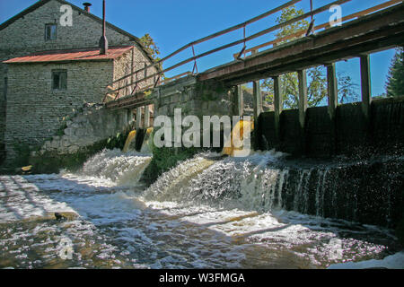 Barrage à l'ancien moulin à eau en pierres. Beaux jets d'eau, une petite chute. Sur le barrage est un vieux pont de bois. Clair bleu ciel. Banque D'Images