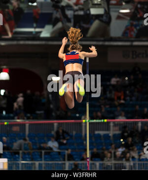 Une école du triple saut féminin, athlète, est bien au-dessus de la barre à un concours dans une patinoire. Banque D'Images