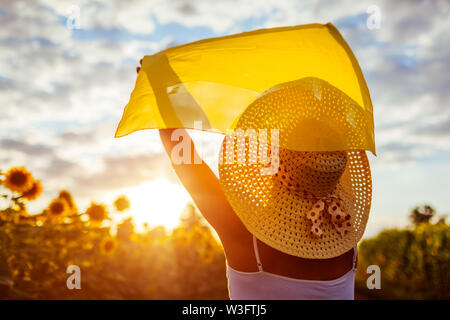 Happy senior woman walking in blooming champ de tournesol élever les mains à l'écharpe et s'amusant. Vacances d'été. Banque D'Images