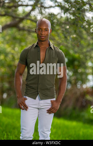 Beau mâle model posing dans le parc. Portrait of African American guy dans des vêtements décontractés et les pouces dans les poches Banque D'Images