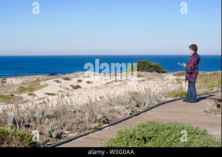 Femme à l'écoute de la bande audio d'enseignement sur la voie de la promenade, les dunes côtières et l'océan Pacifique, Parc d'état d'Asilomar, Pacific Grove, California, USA Banque D'Images