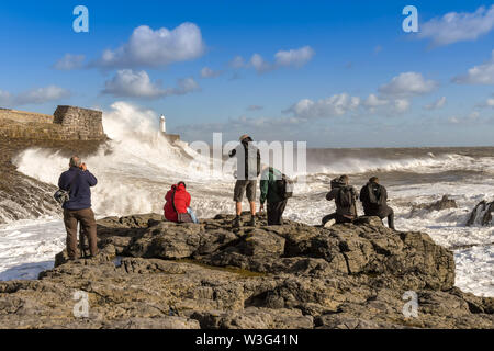 PORTHCAWL, EALES - Octobre 2018 : Groupe de personnes sur des roches à prendre des photos de grandes vagues sur la marée montante se briser contre le mur du port. Banque D'Images