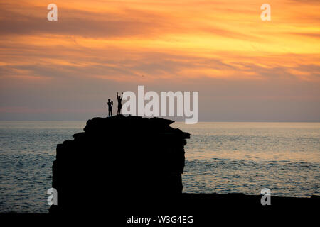 Portland Bill, Dorset, UK. 15 juillet, 2019. Deux personnes admirer le coucher de soleil depuis le haut de Pulpit Rock sur Portland Bill, Dorset, après une journée sans nuages sur la côte sud-ouest de la Grande-Bretagne. Peter Lopeman/Alamy Live News Banque D'Images