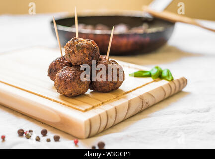 Les boulettes de viande sur une planche en bois avec des cure-dents contre fond blanc Banque D'Images