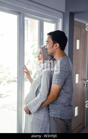 Femme musulmane enceinte appuyée sur la poitrine de mari romantique à la maison Banque D'Images