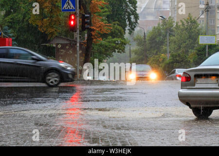 Les eaux de pluie torrentielles voitures passant au carrefour de la route et la lumière rouge de la lumière est reflétée dans l'écoulement de l'eau sur une ville s Banque D'Images