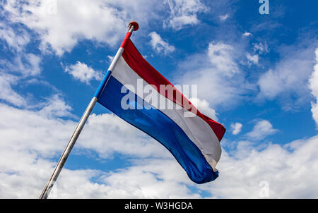 Drapeau des Pays-Bas. Symbole national néerlandais agitant sur perche contre ciel bleu avec des nuages, journée ensoleillée Banque D'Images